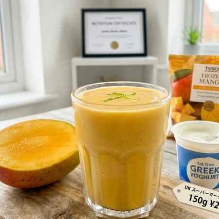 Weight Loss Smoothies: 6 Nutritionist Approved Recipes for UK Kitchens A close-up photograph of a vibrant, orange mango smoothie in a clear glass tumbler, sitting on a rustic wooden board. Adjacent to the glass is a half-peeled ripe mango and a small pot of plain Greek yoghurt.