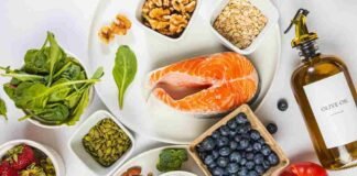 Flat lay of the best anti-inflammatory foods including salmon, berries, walnuts, spinach and turmeric on a marble surface